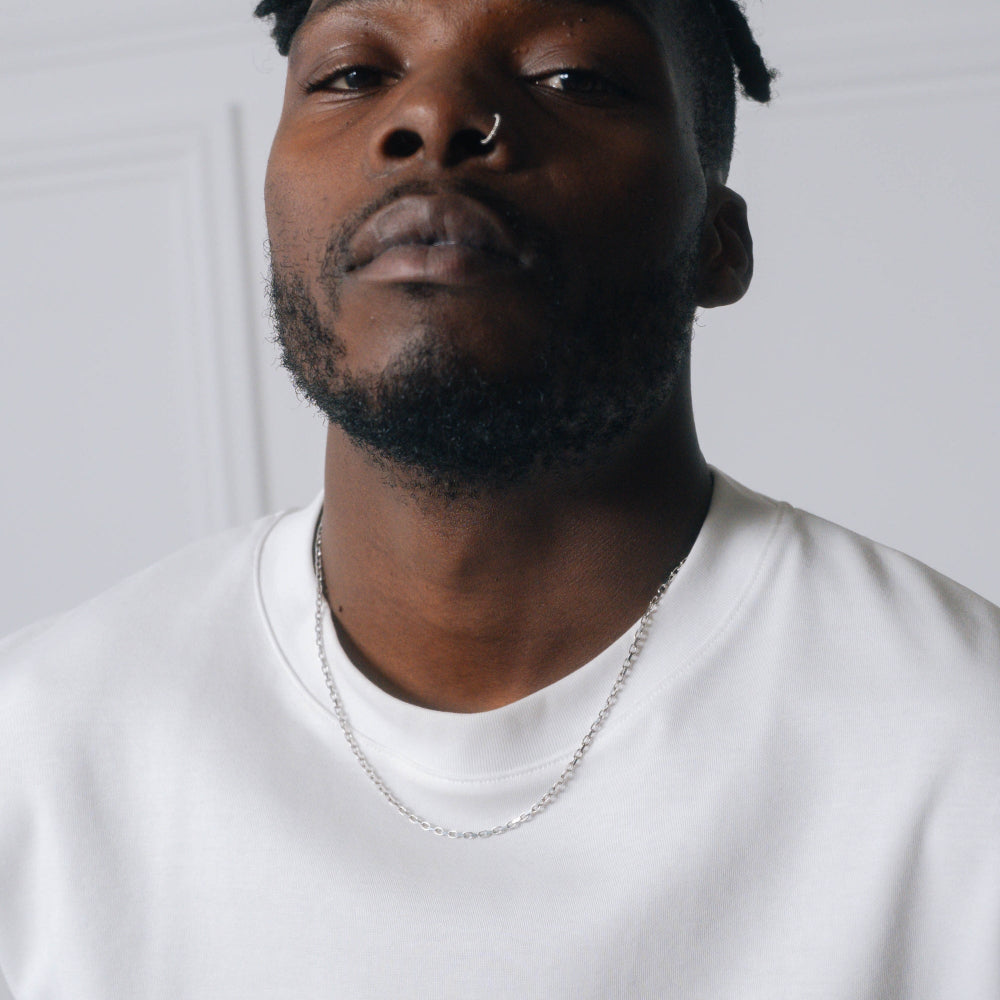 Man wearing a white t-shirt and silver chain necklace against a plain background