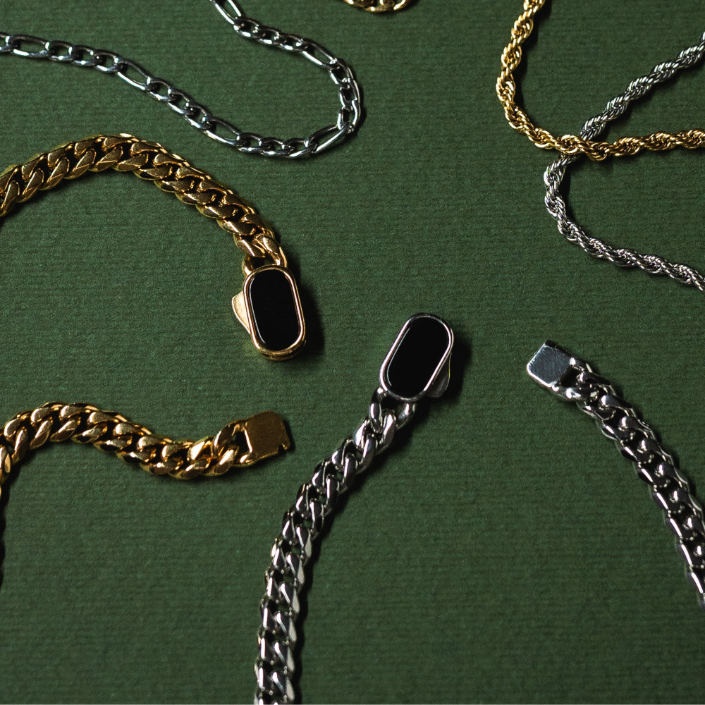 Gold, silver, and black chain necklaces on a green background