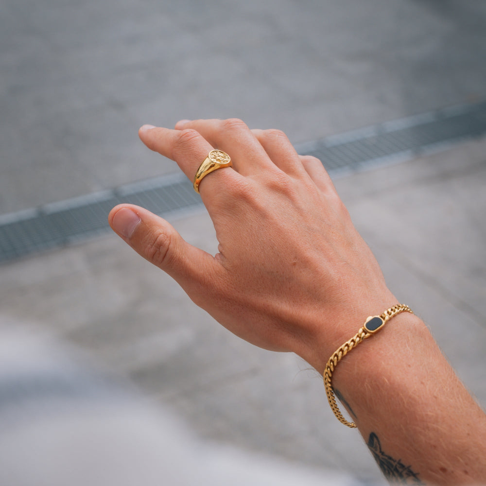 Hand wearing a gold ring and bracelet on a blurred background