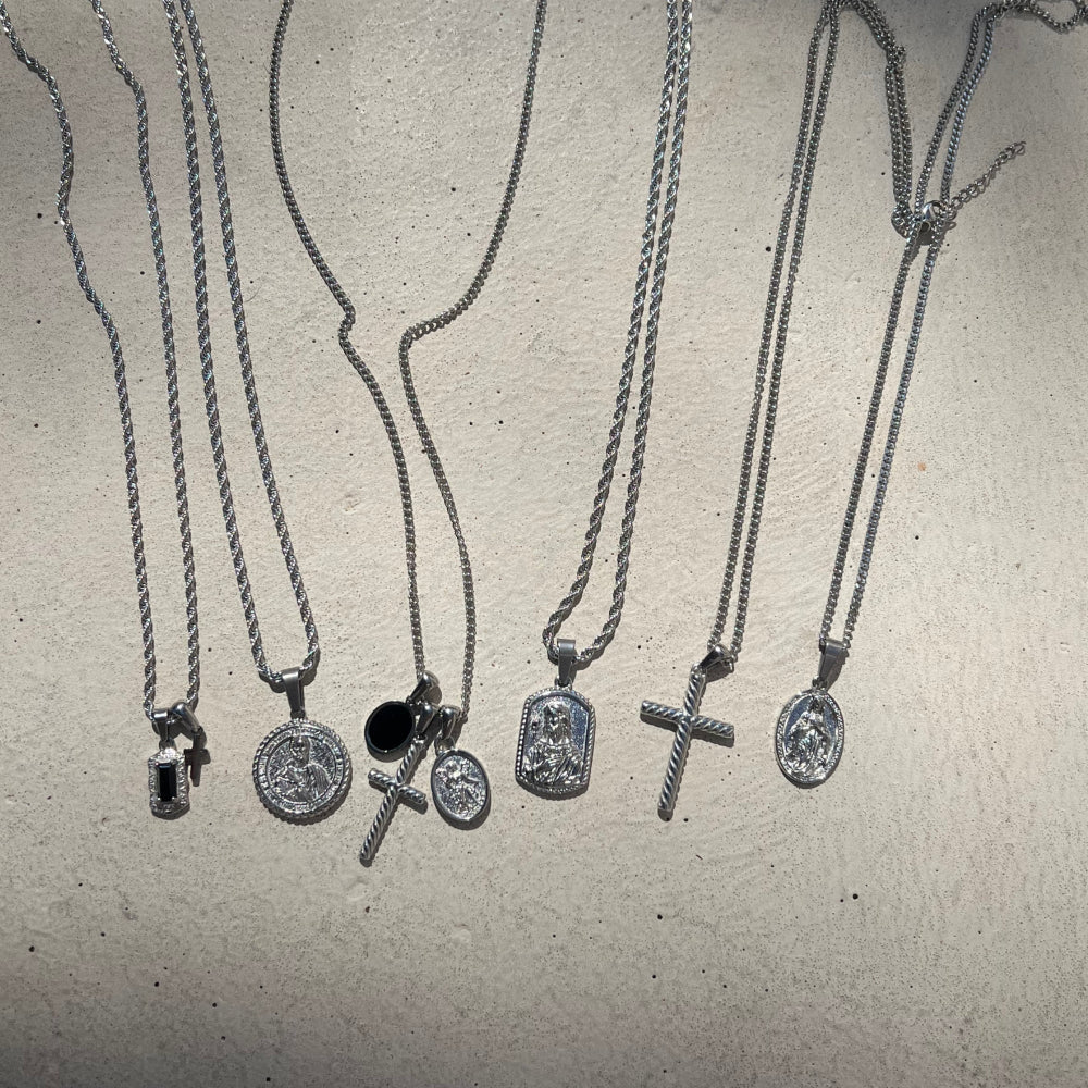 Collection of silver necklaces with various pendants on a textured surface