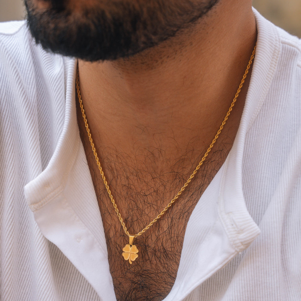 Gold necklace with a clover pendant worn by a person in a white shirt.