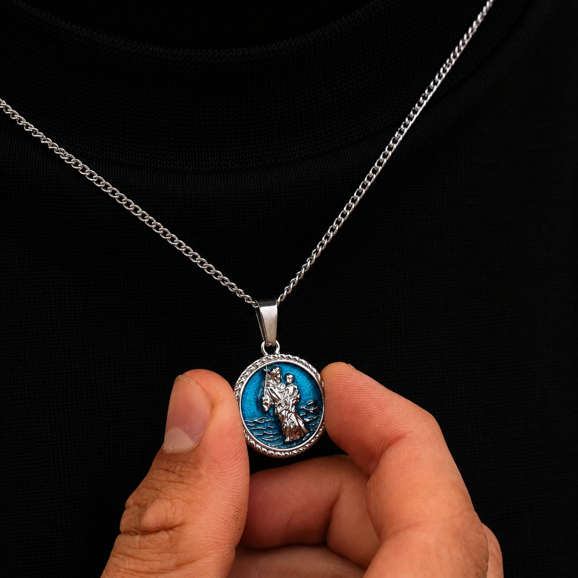 Hand holding a necklace with a blue pendant against a black background