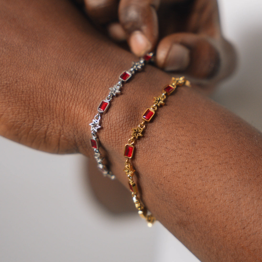 Two bracelets, one gold and one silver with red stones, on a wrist.