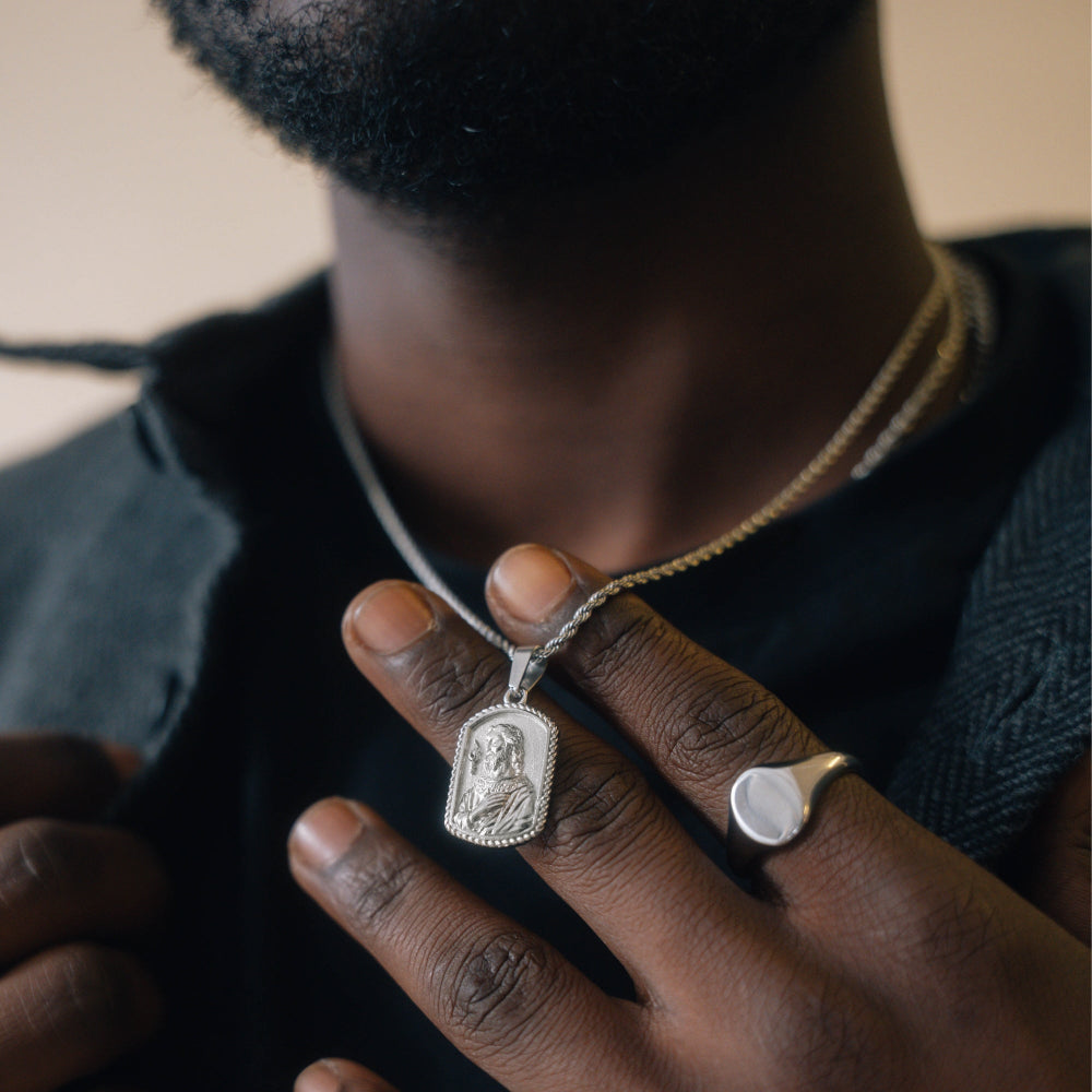 Person wearing a silver necklace with a pendant, holding it with their hand.