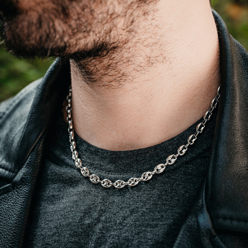 Close-up of a person wearing a silver chain necklace with a blurred background