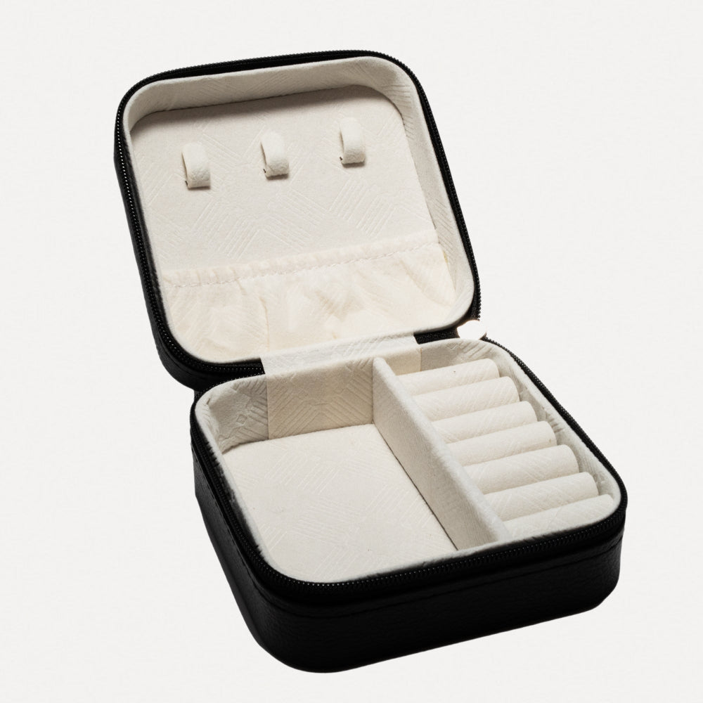 Black jewelry case with white interior, containing earrings and rings, on a white background