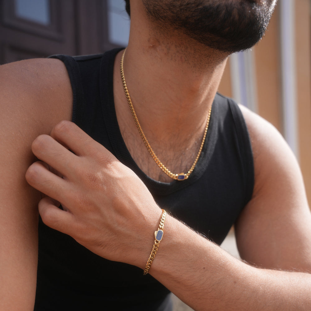 Person wearing a gold chain necklace and bracelet, with a blurred background