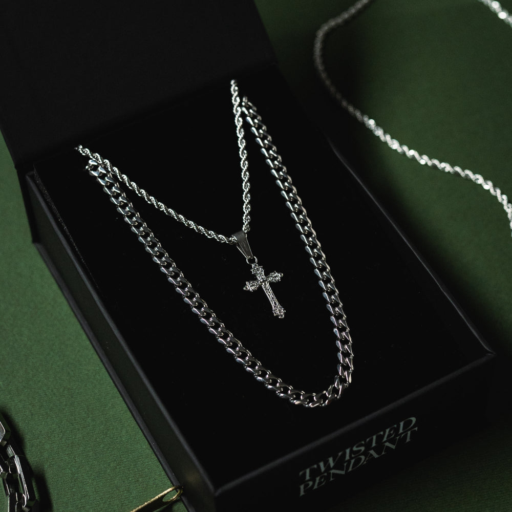 Silver chain necklace with a cross pendant on a black box labeled 'Twisted Pendant'.
