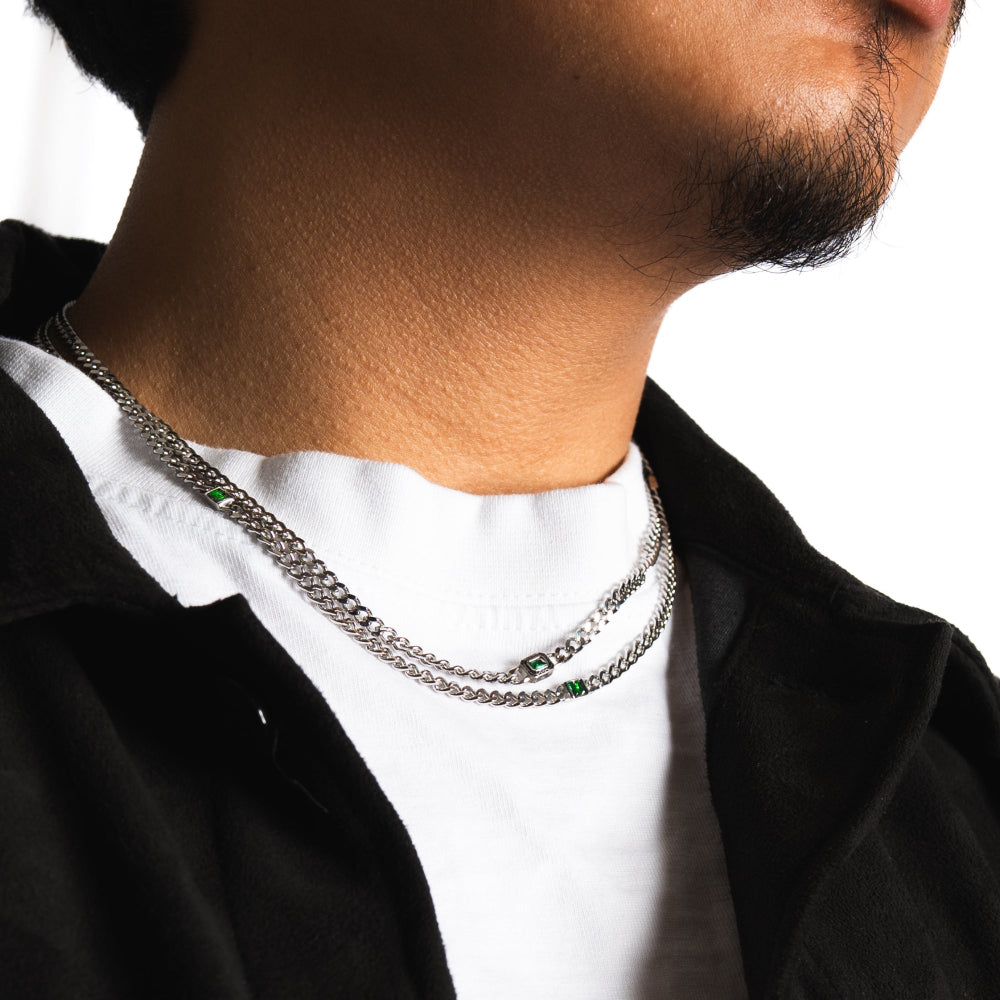 Person wearing a silver chain necklace with a white shirt and black jacket.