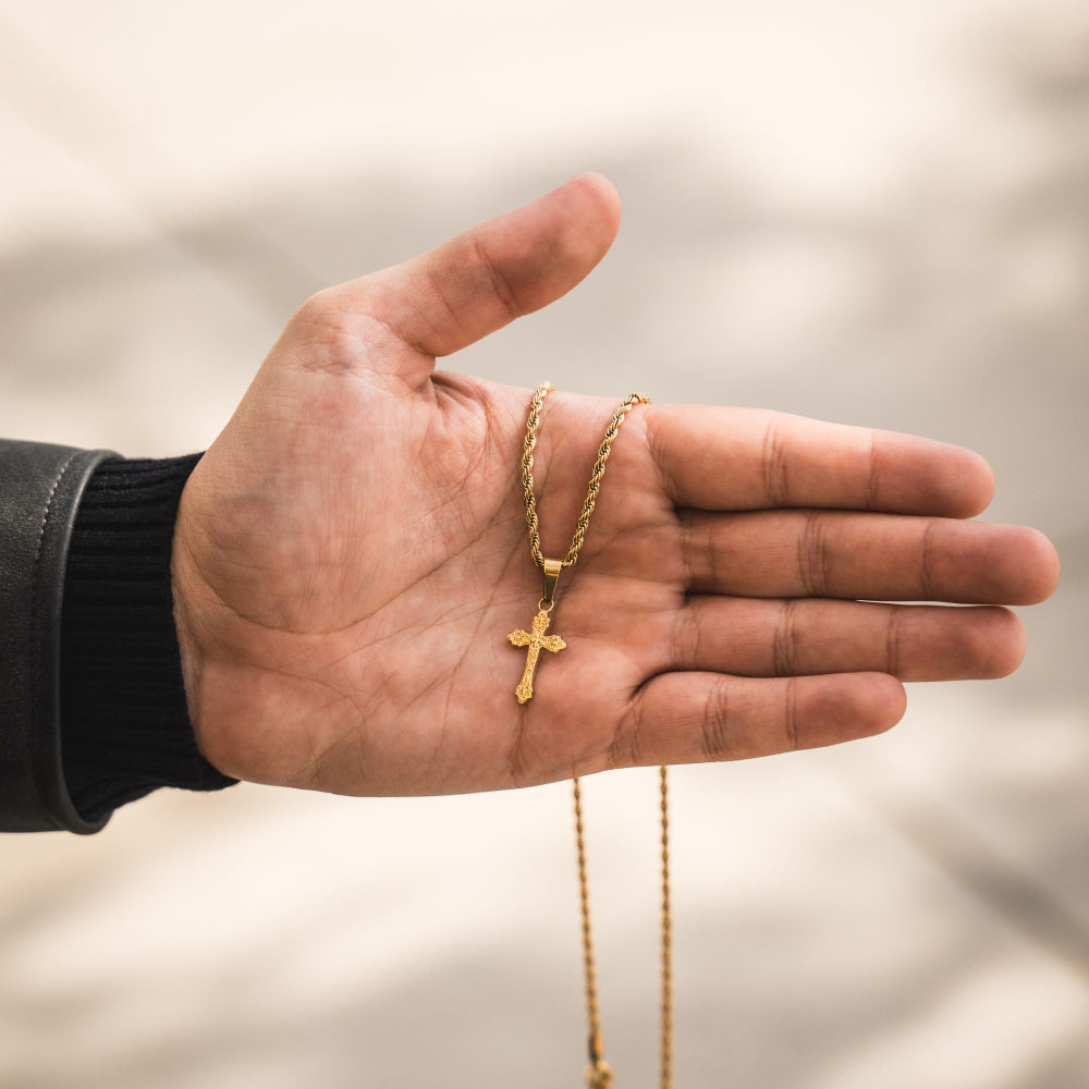 Gold cross necklace on a hand with a blurred background