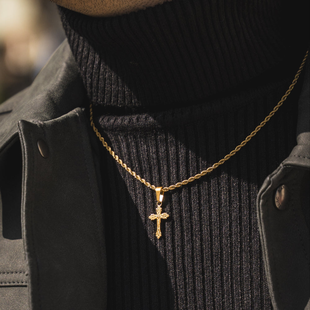 Gold necklace with a cross pendant worn by a person in a black coat and turtleneck.