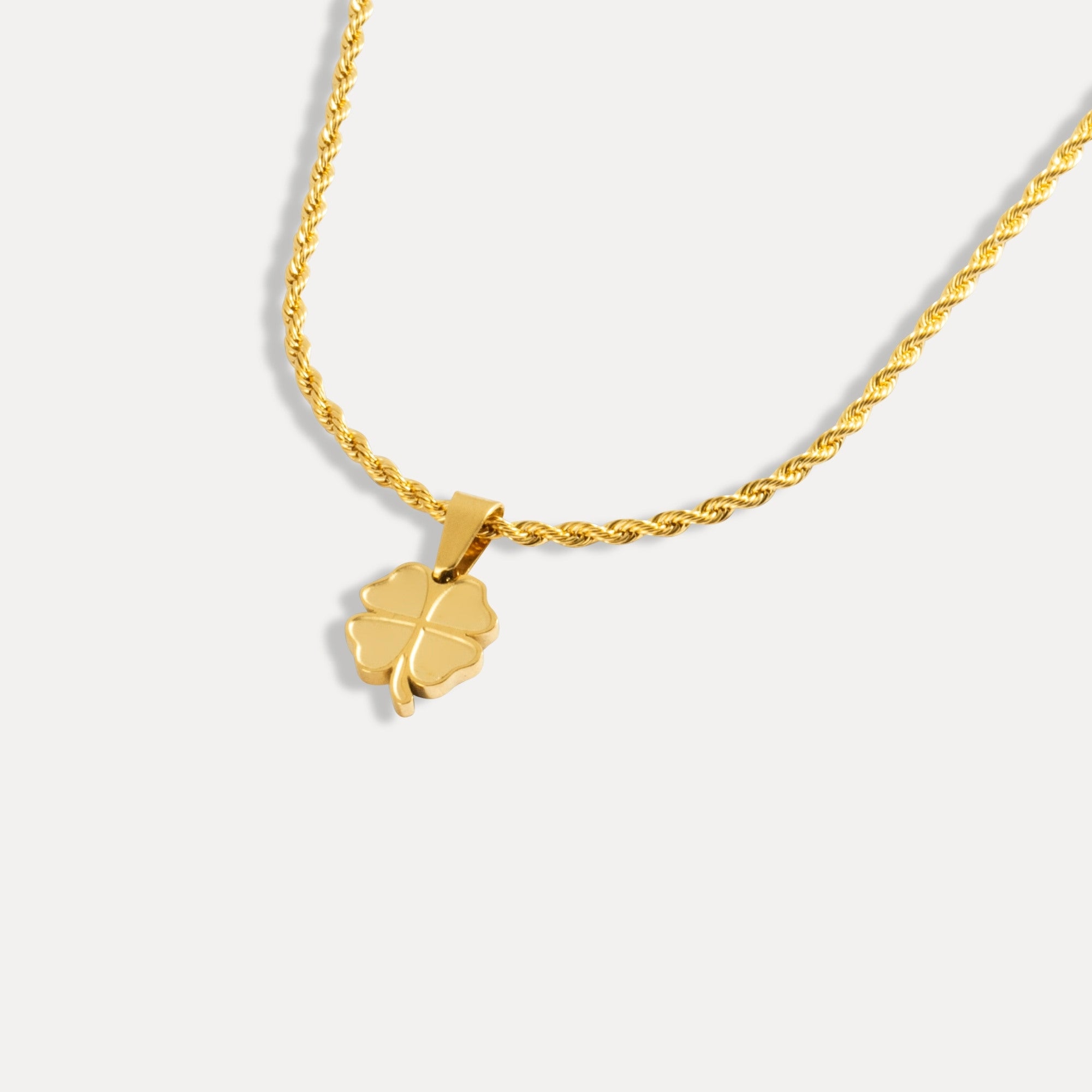 Gold necklace with a clover-shaped pendant on a light gray background