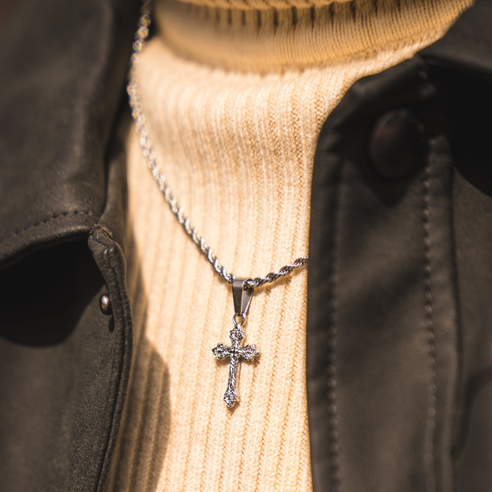 Silver cross necklace on a person wearing a beige sweater and dark jacket.