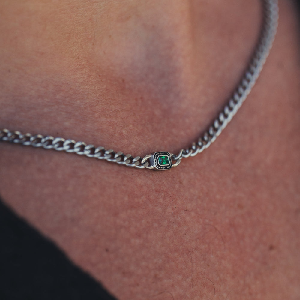 Close-up of a silver chain necklace with a green gemstone on a person's neck.