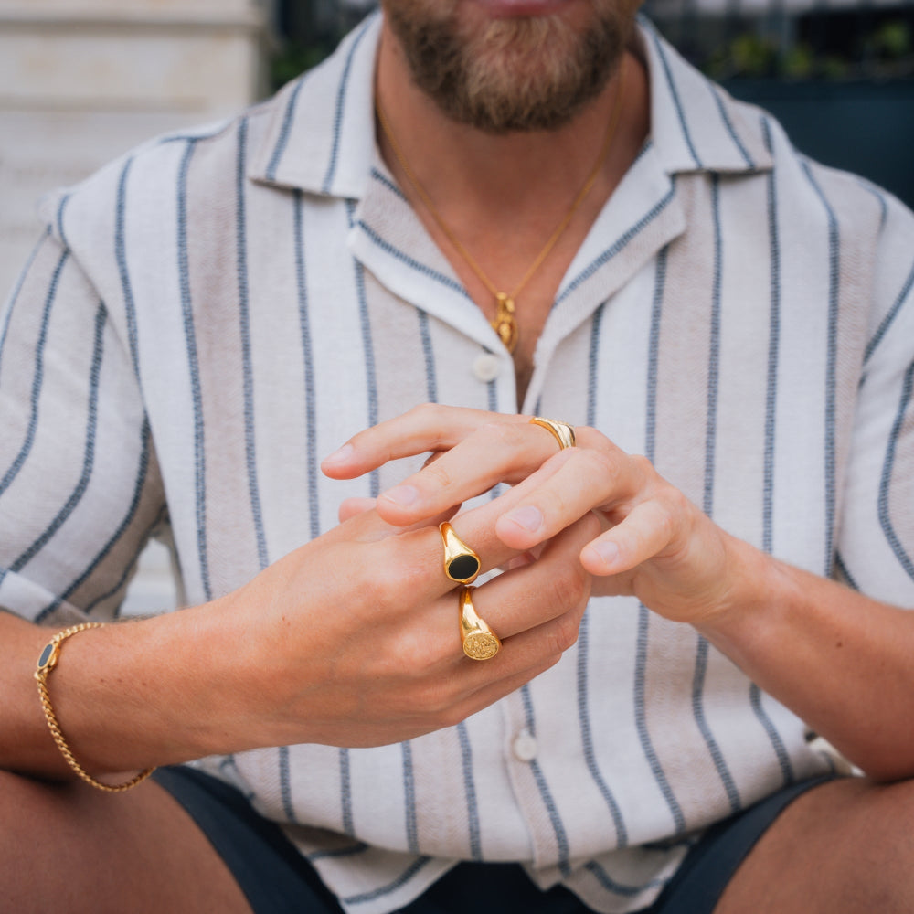 Person wearing gold rings on fingers with a striped shirt in the background