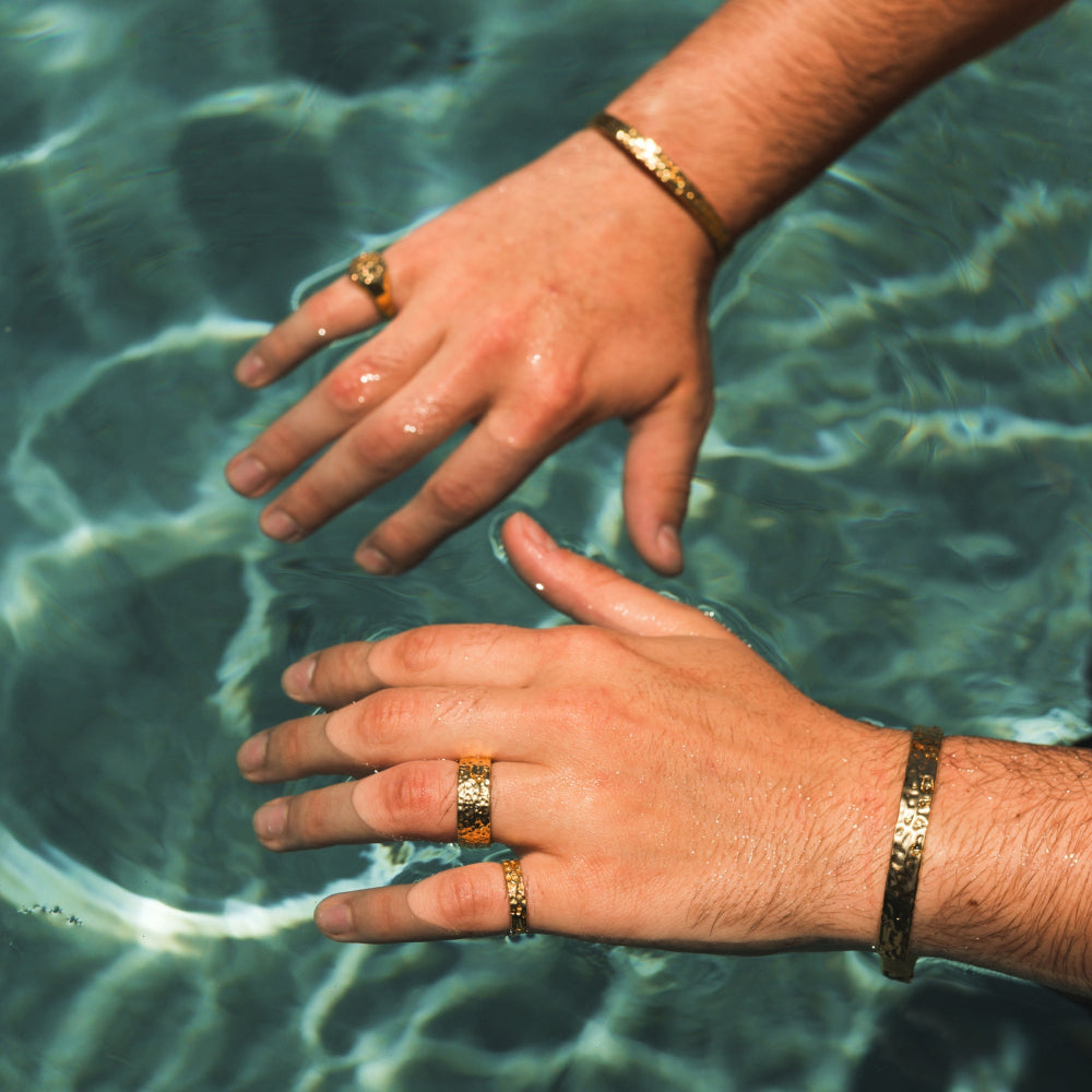Two hands with gold rings and bracelets touching water