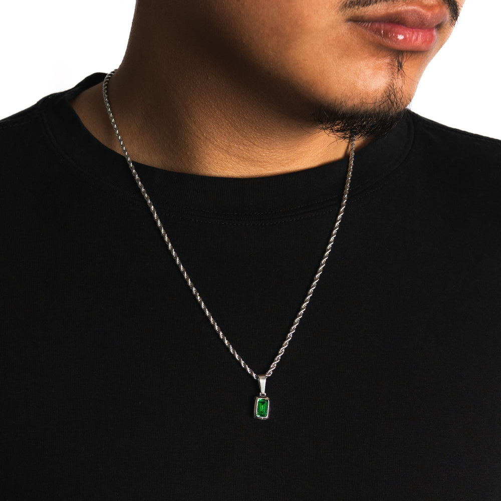 Man wearing a black shirt with a silver necklace featuring an emerald pendant.