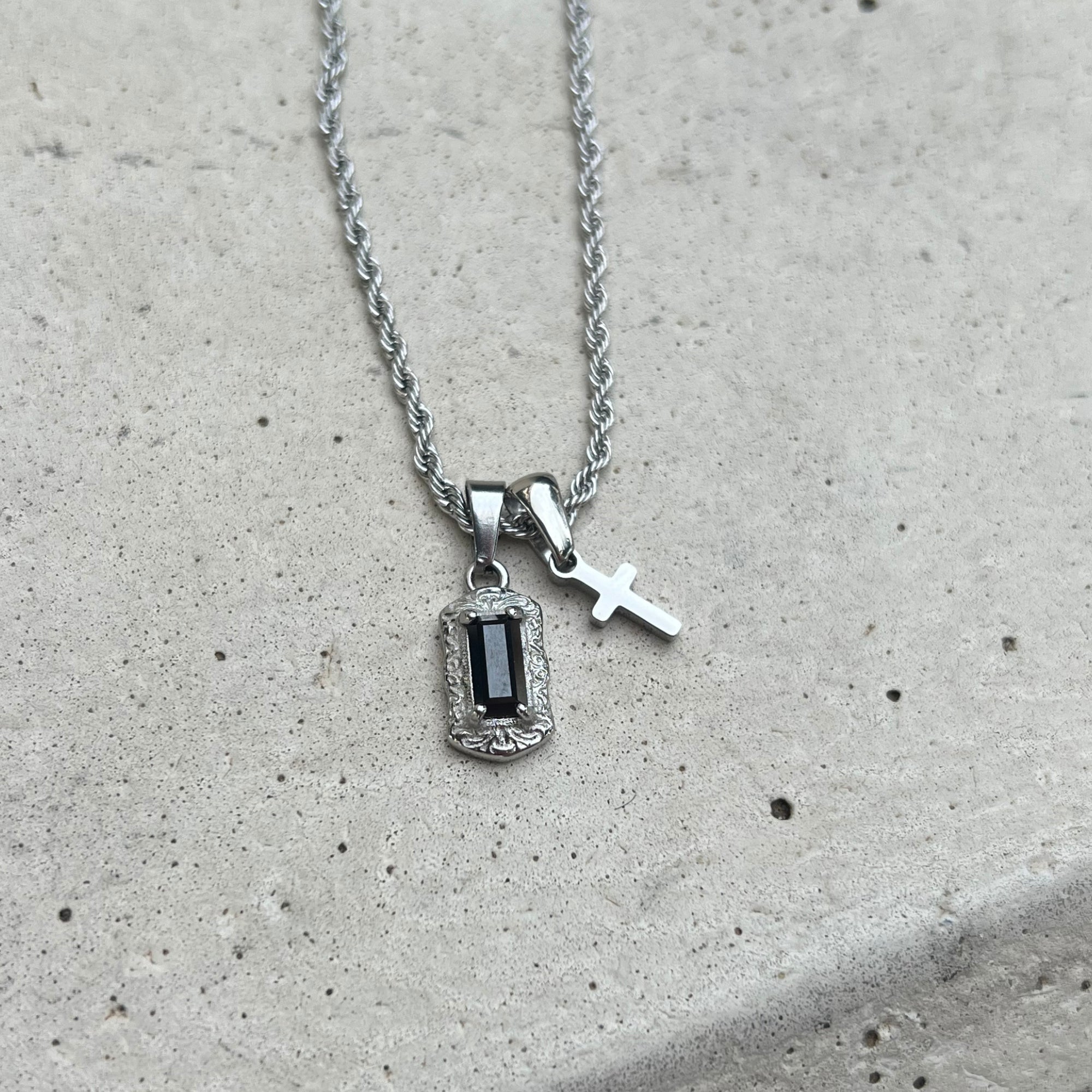 Silver necklace with pendant and cross on a concrete surface