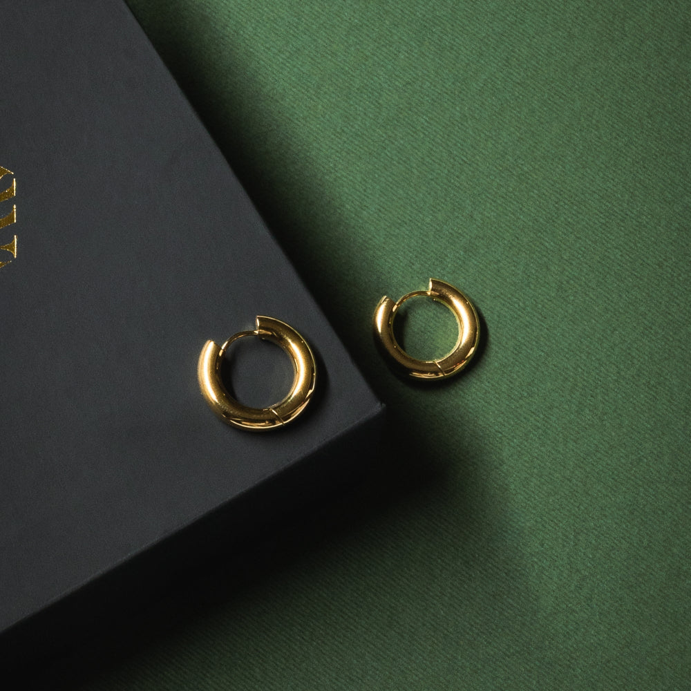 Gold hoop earrings on a dark green surface