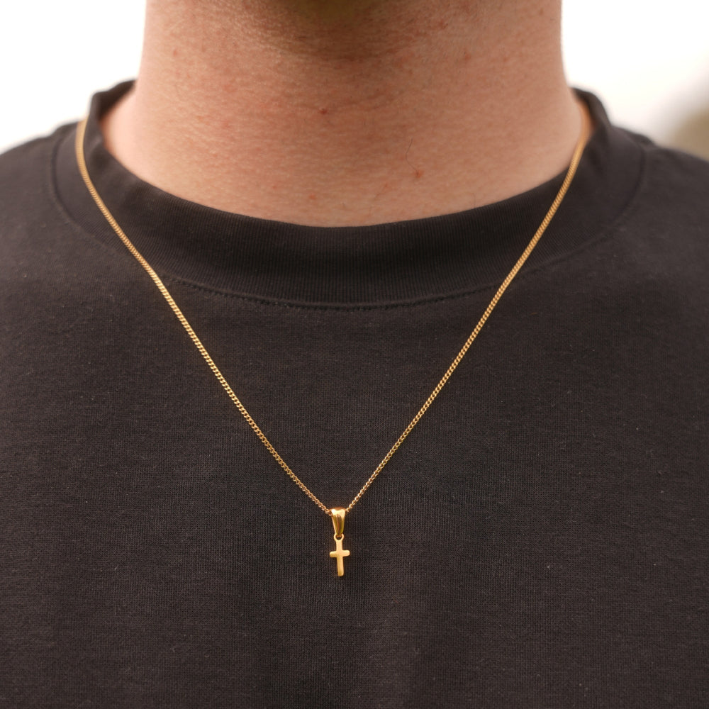 Gold necklace with a cross pendant on a person wearing a black shirt.