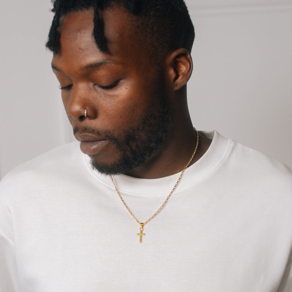 Man wearing a gold necklace with a cross pendant on a plain background