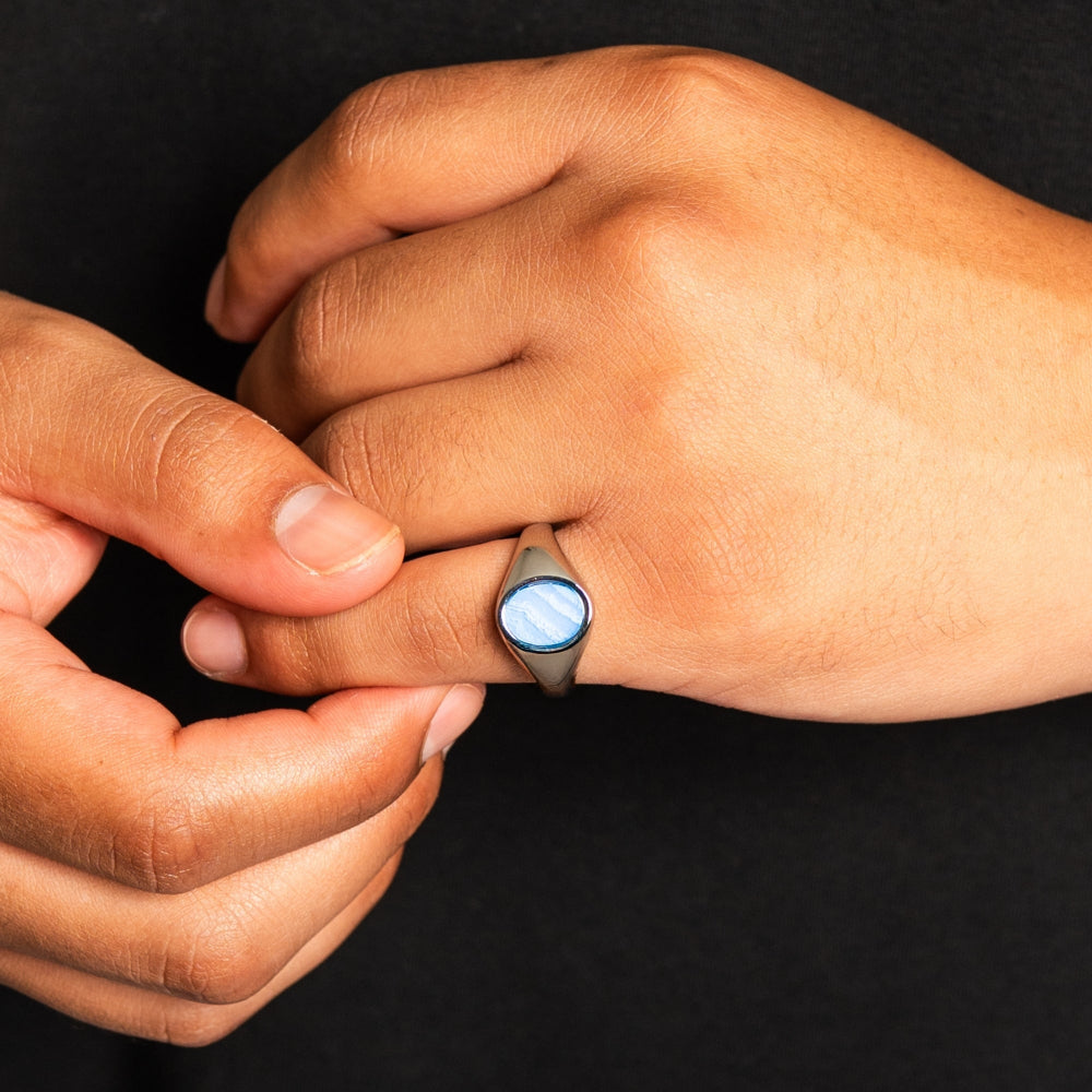 Close-up of a hand wearing a ring with a glowing blue stone against a black background