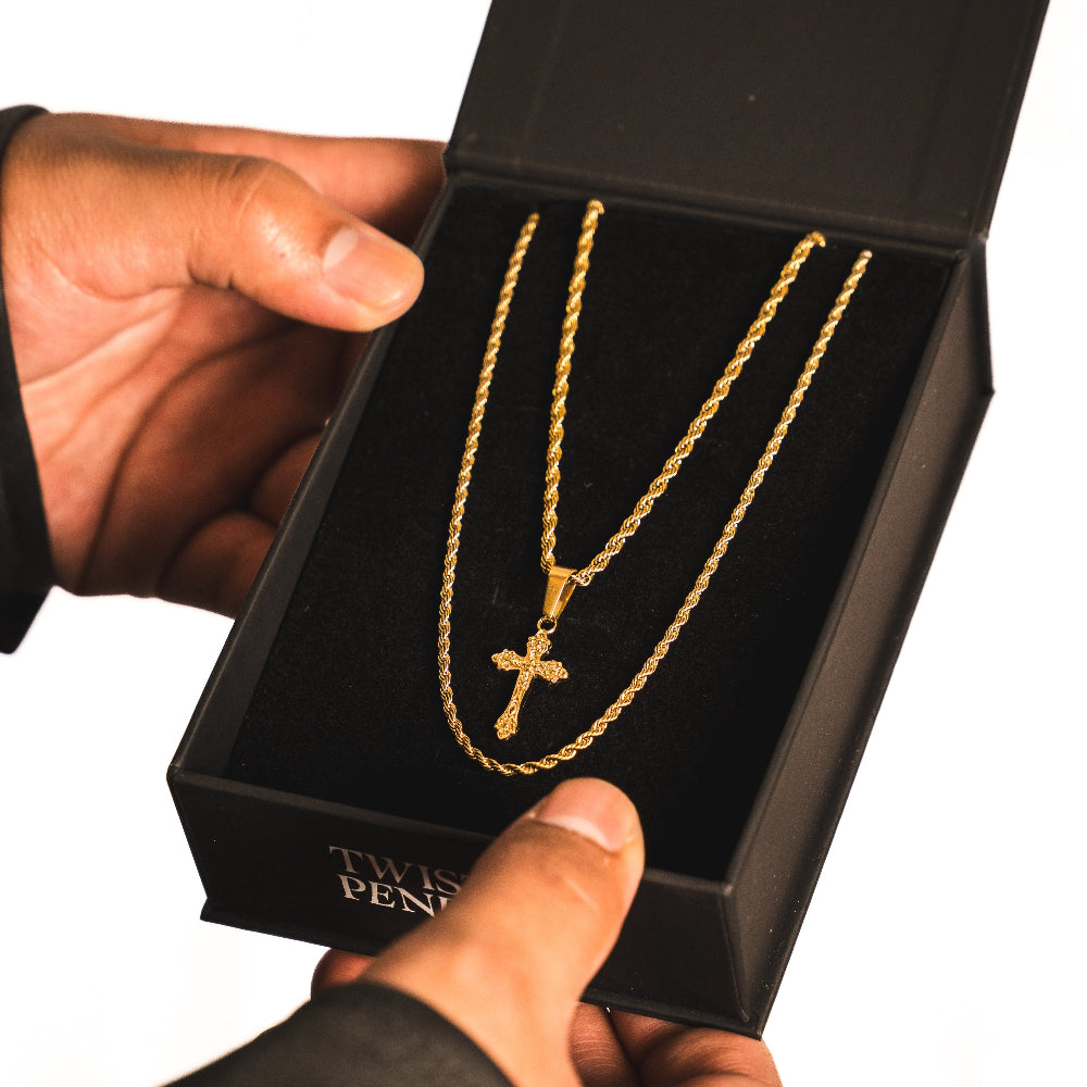 Gold necklace with a cross pendant in a black box held by a hand.