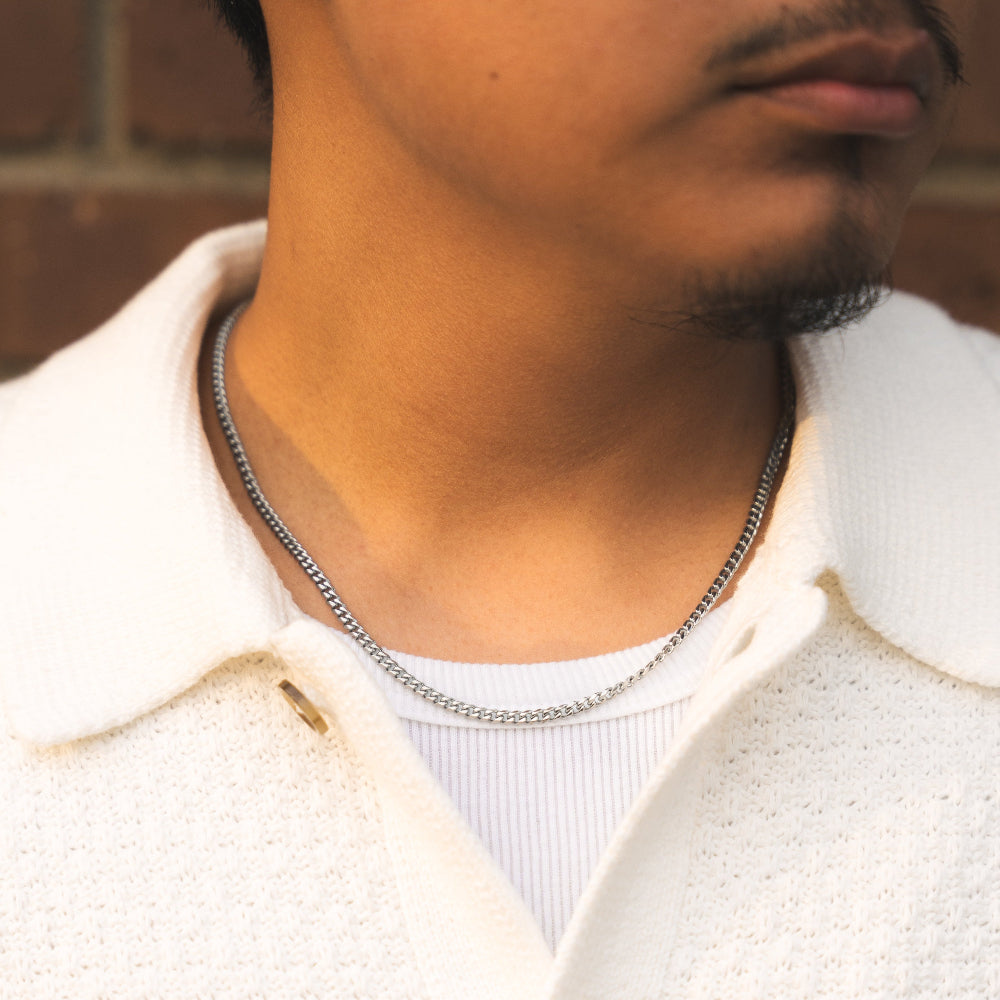 Close-up of a person wearing a white textured shirt with a collar and a silver chain necklace.