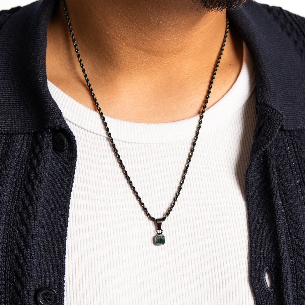 Person wearing a black chain necklace with a pendant on a white shirt and dark jacket.