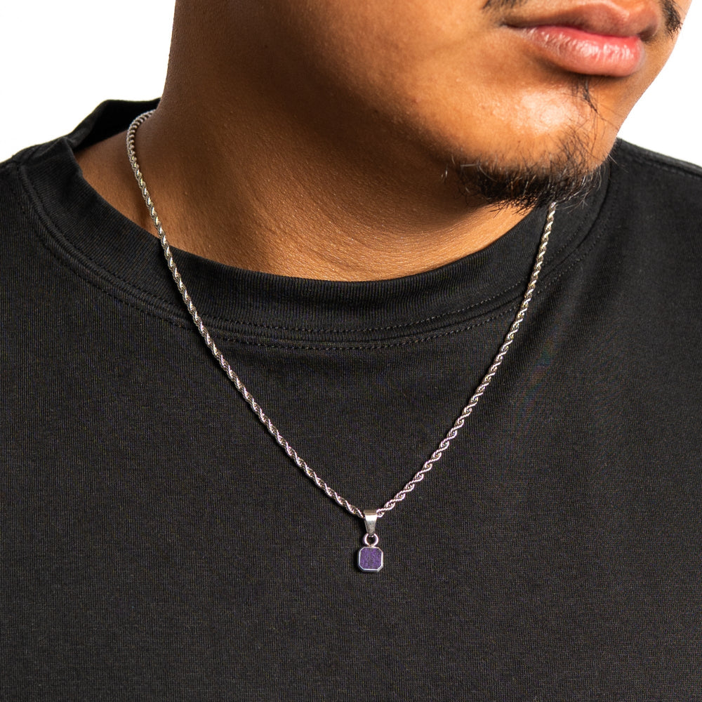 Man wearing a black shirt with a silver necklace featuring a purple pendant.