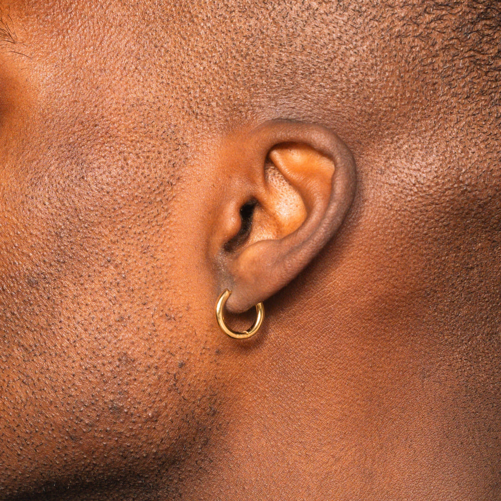 Close-up of an ear with a gold hoop earring on a brown skin background