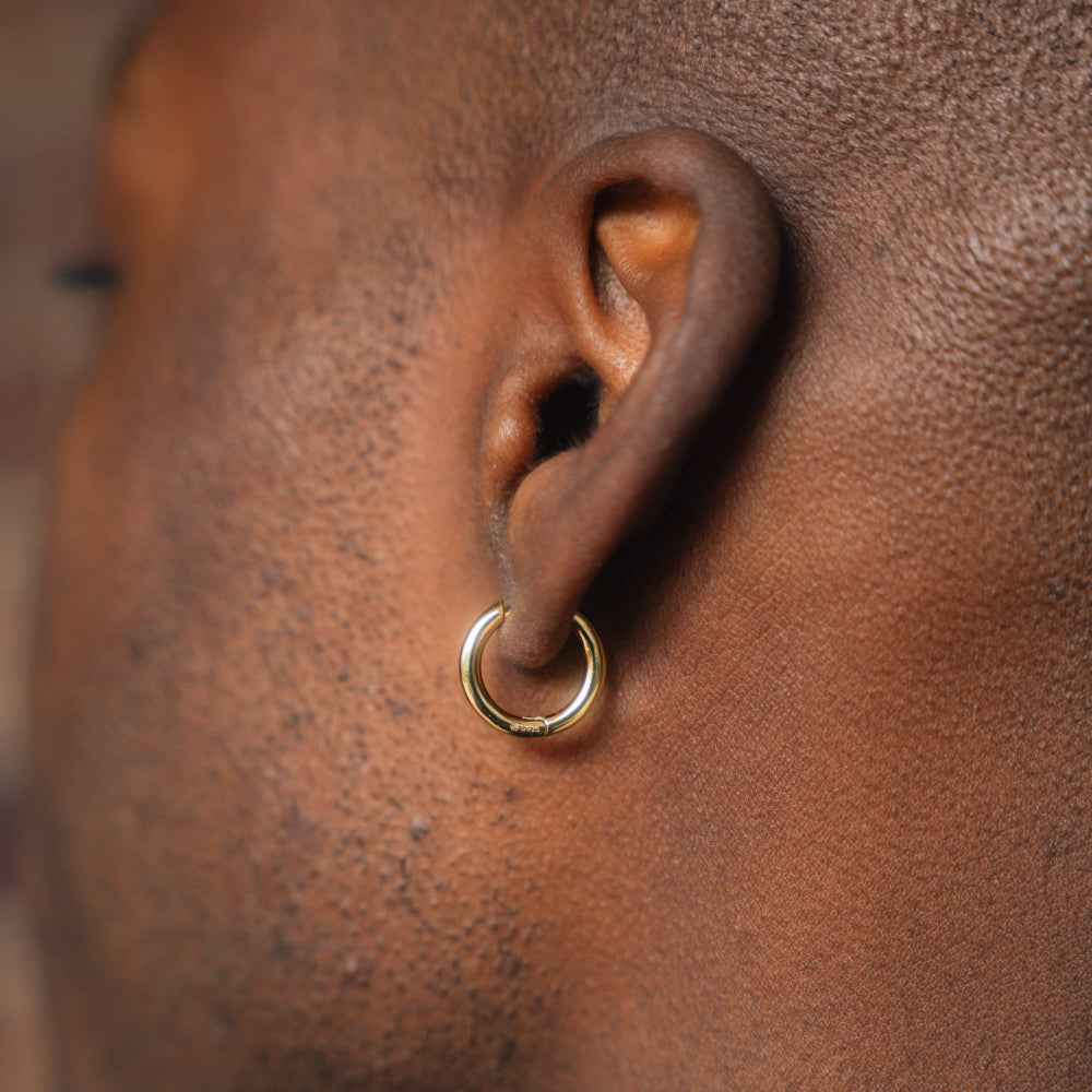 Close-up of an ear with a gold hoop earring on a brown background