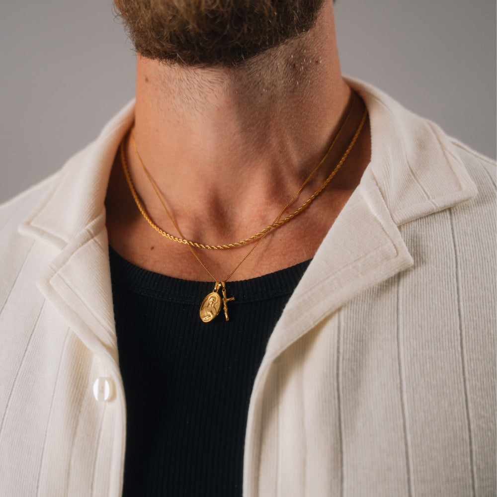 Man wearing a gold necklace with two pendants against a neutral background