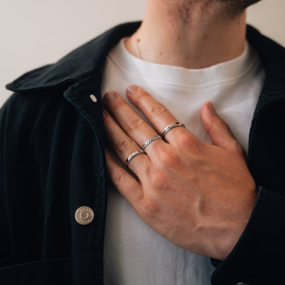 Person wearing a black jacket with a button, white shirt, and multiple rings on fingers.
