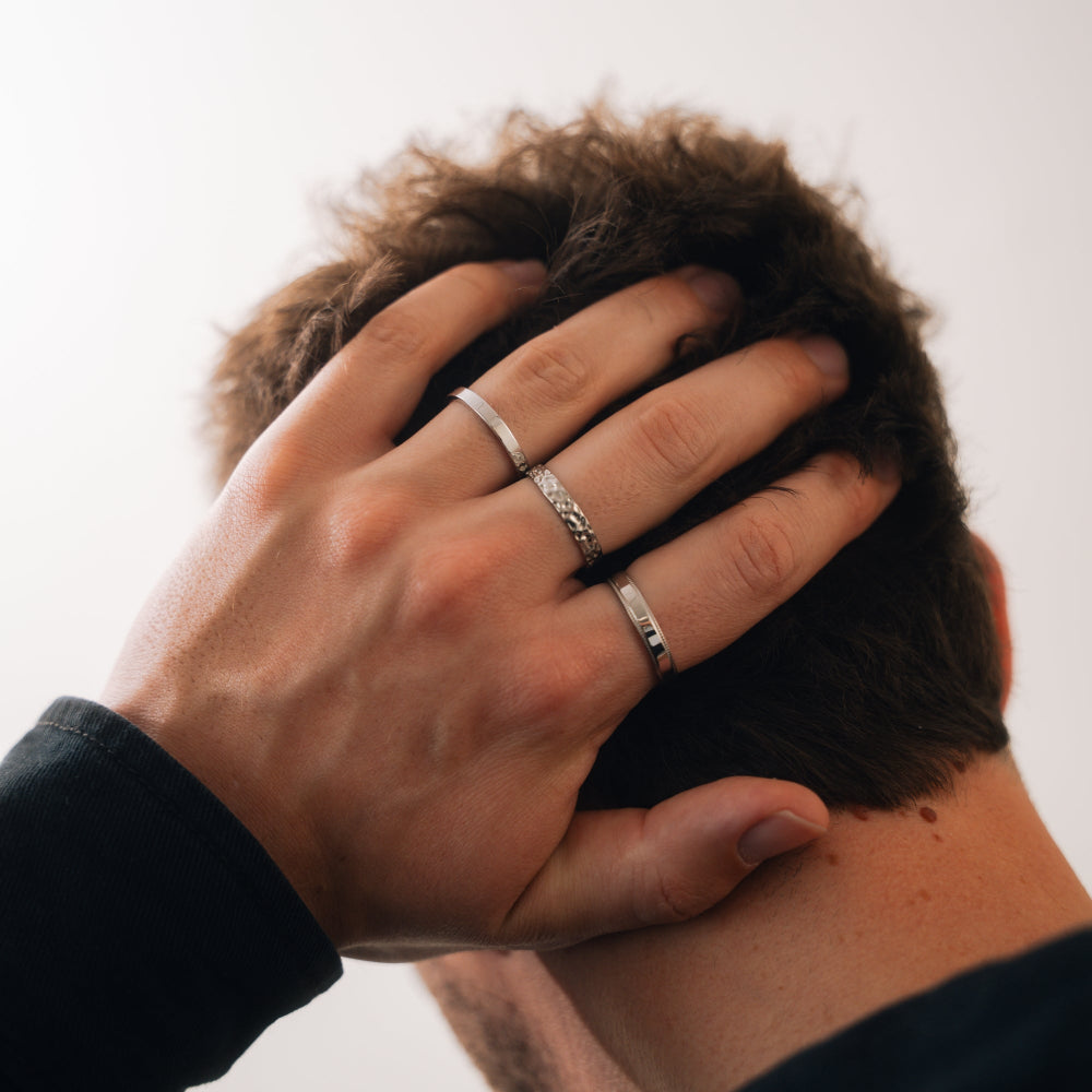 Hand with multiple rings on a person's head against a neutral background