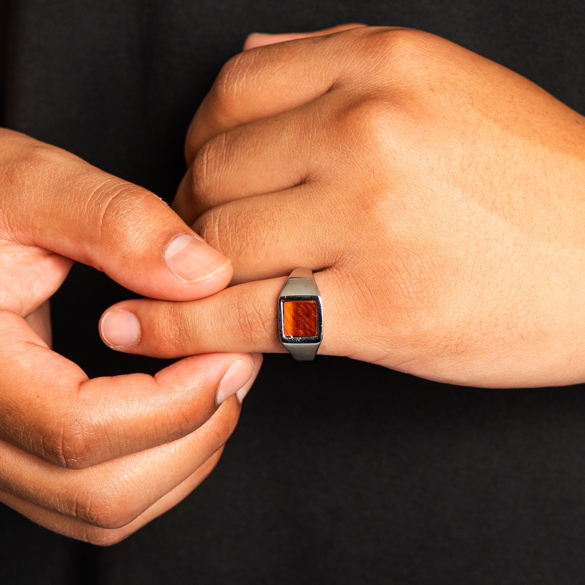 Close-up of a hand wearing a ring with a red stone, held by another hand against a black background
