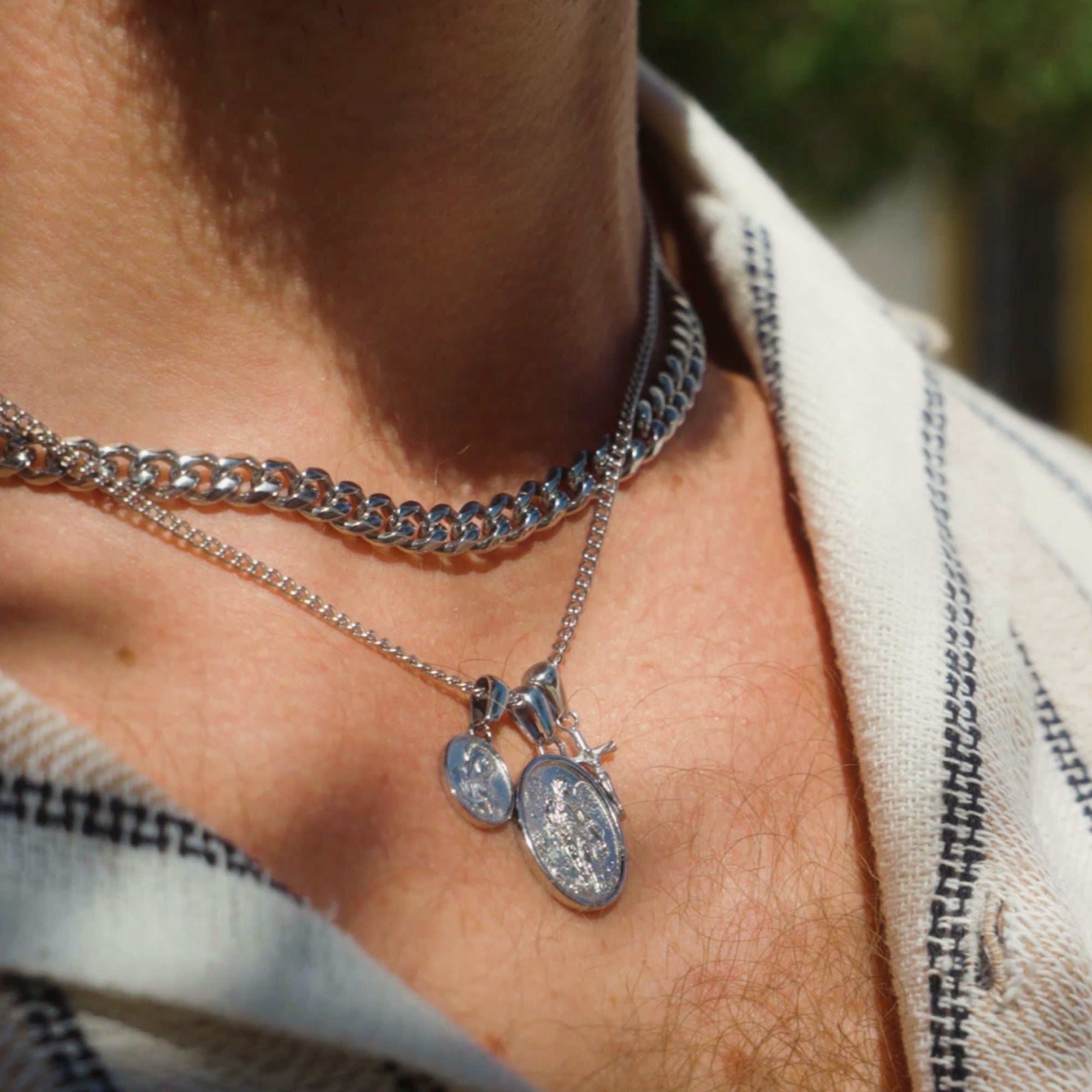 Close-up of a person wearing multiple silver necklaces with pendants.