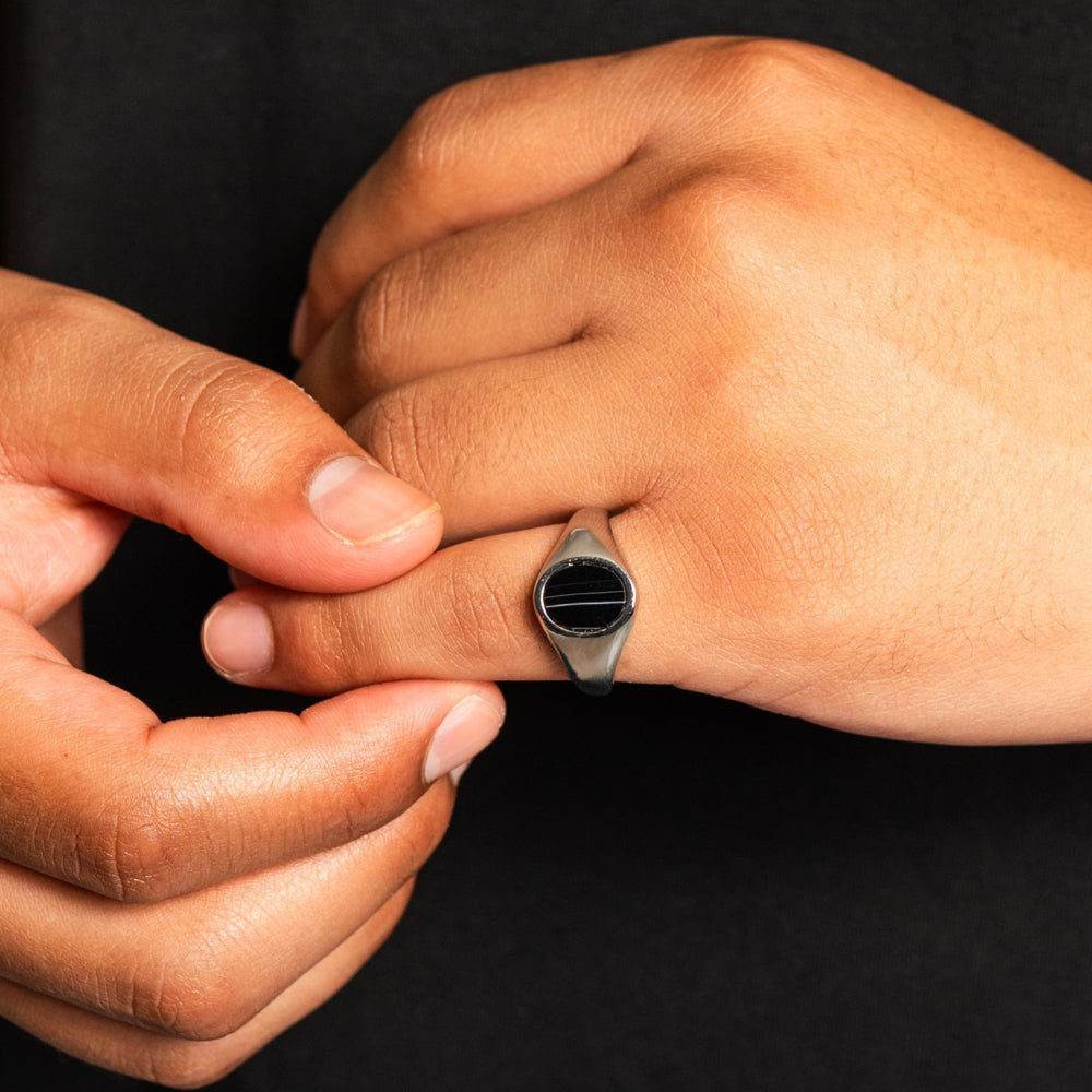 Close-up of a hand wearing a silver ring with a black stone on a dark background