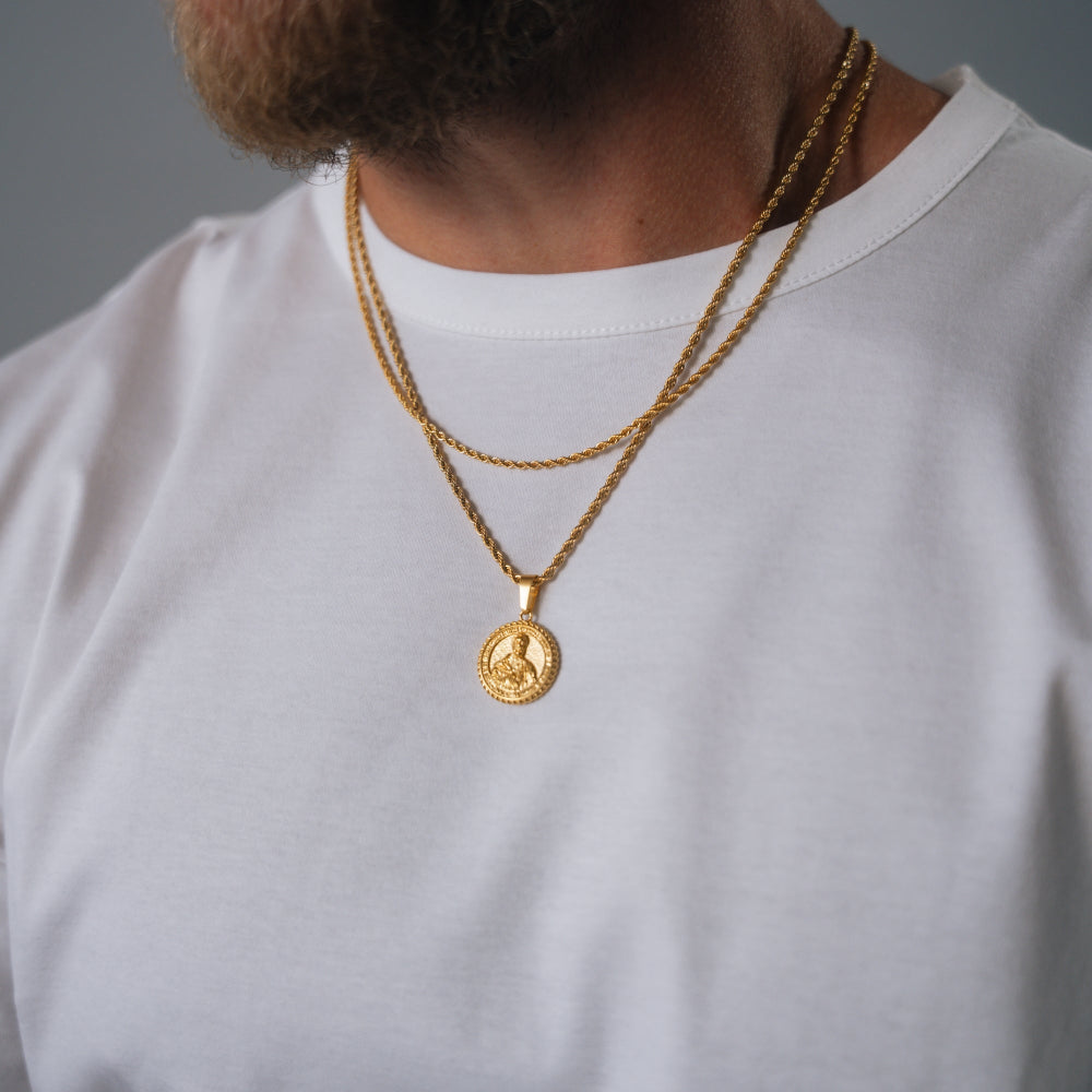 Gold necklace with a pendant on a person wearing a white shirt against a gray background